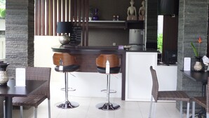 A modern bar area with two stools, a refrigerator, and decorative items. - Griya Nendra Hotel (Ngaglik)
