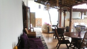 A covered outdoor seating area with wooden furniture and a woven chair. - Griya Nendra Hotel (Ngaglik)