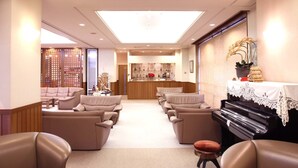 Un amplio salón con sofás de cuero, un piano y un mostrador de recepción al fondo.