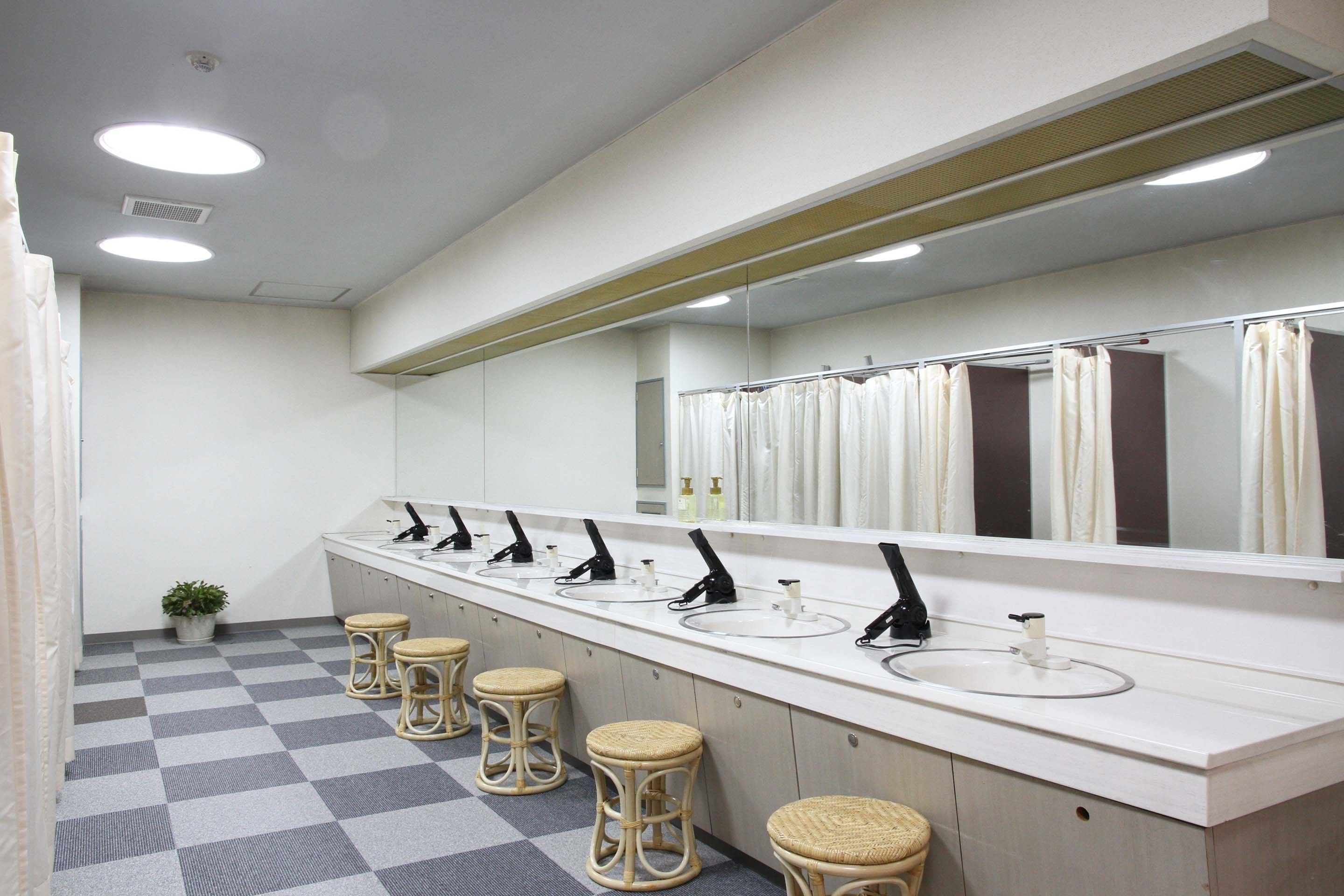 Un baño público con varios lavamanos, espejos y taburetes.