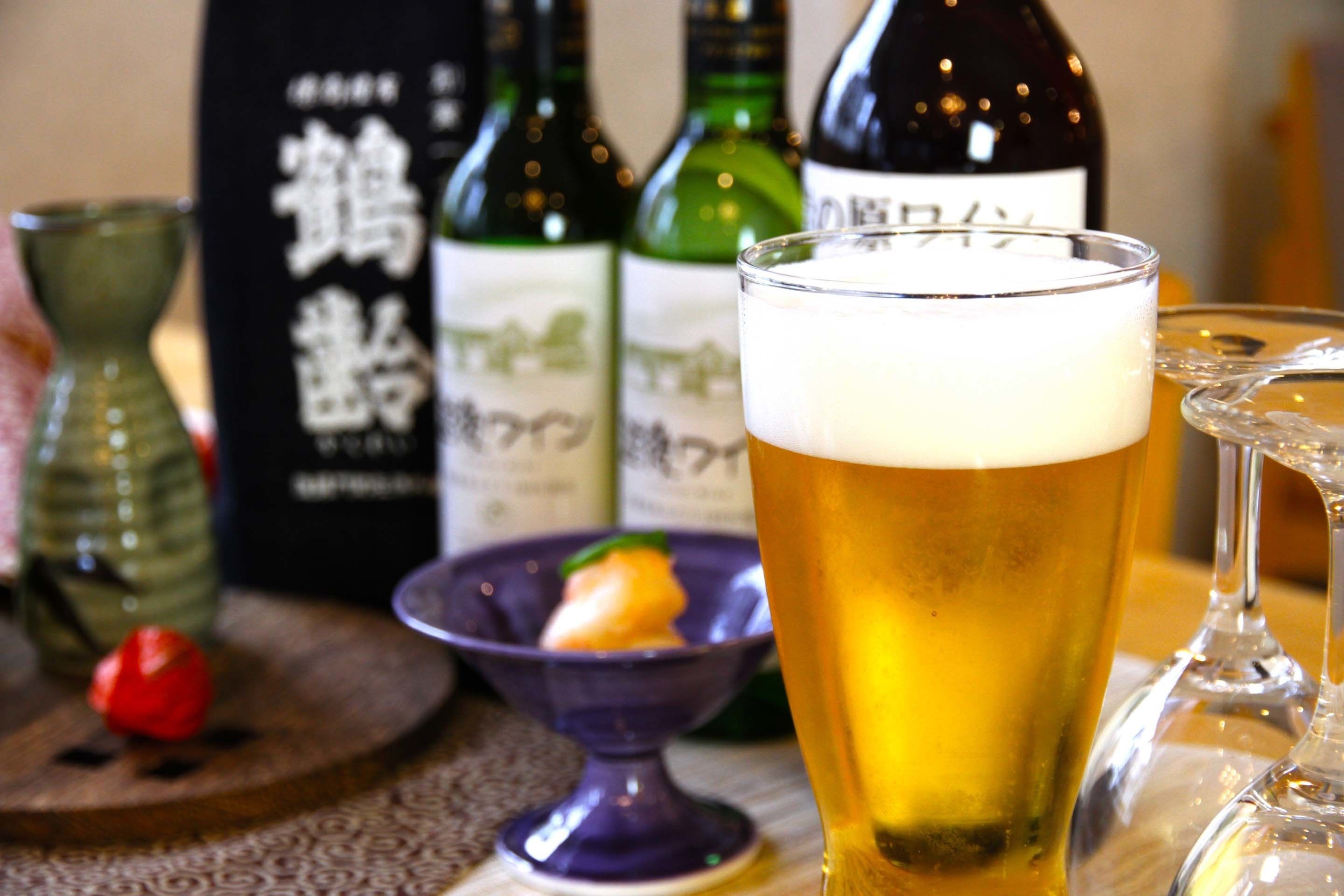 A glass of beer with a frothy head, a bottle of beer, and a small bowl with a garnish on a wooden table.