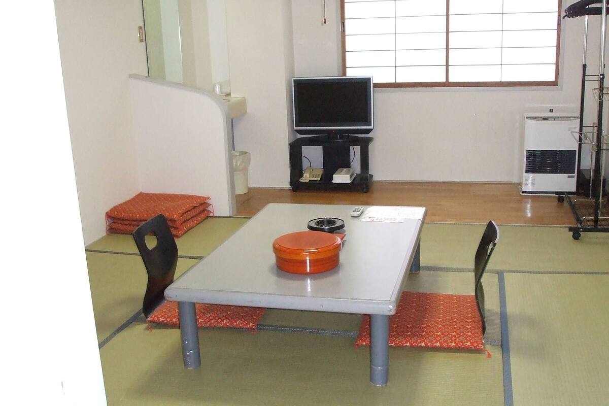 A small room with a table, chairs, a television, and a cart with a heater.