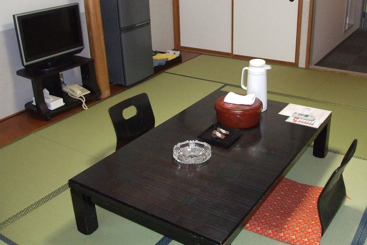 A traditional Japanese-style room with tatami flooring, a low table with a tea set, a television, and a small cabinet.