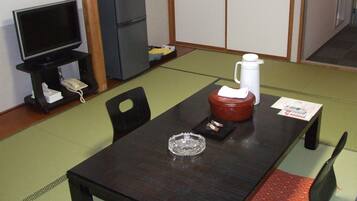 A traditional Japanese-style room with tatami flooring, a low table with a tea set, a television, and a small cabinet.