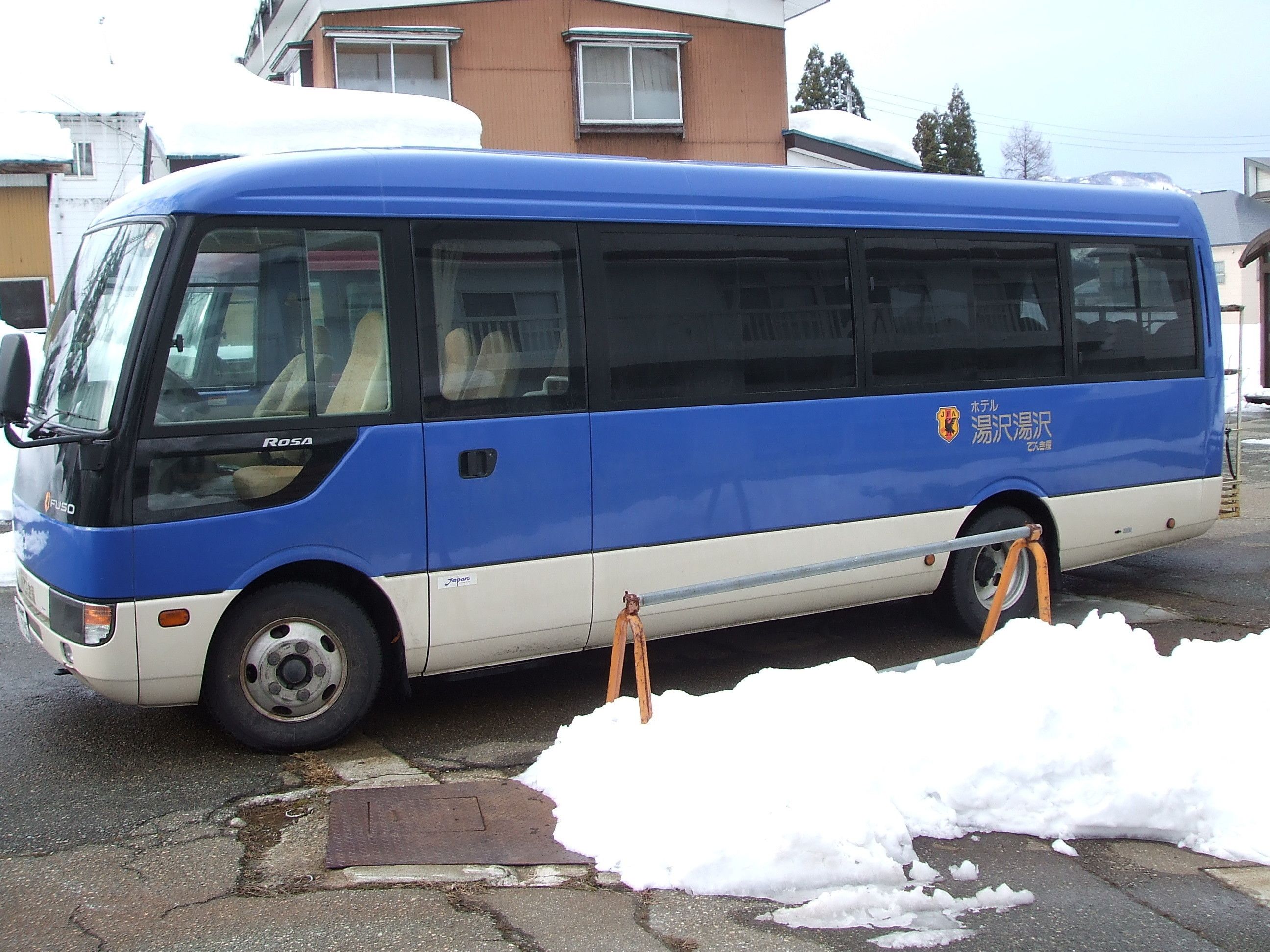A blue and white bus parked on a street with snow on the ground.