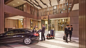 A modern hotel lobby with a car parked in front, a luggage cart, and a man in a suit interacting with a car attendant. - La Vida Hotel (Taichung)