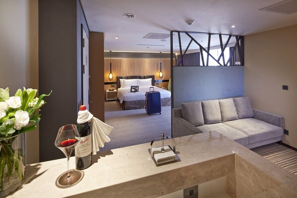 A hotel room with a bed, a sofa, a minibar, a vase with flowers, and a wine glass. - La Vida Hotel (Taichung)