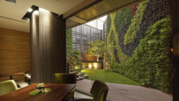 A modern dining area with a wooden table, chairs, and a view of a lush vertical garden. - La Vida Hotel (Taichung)