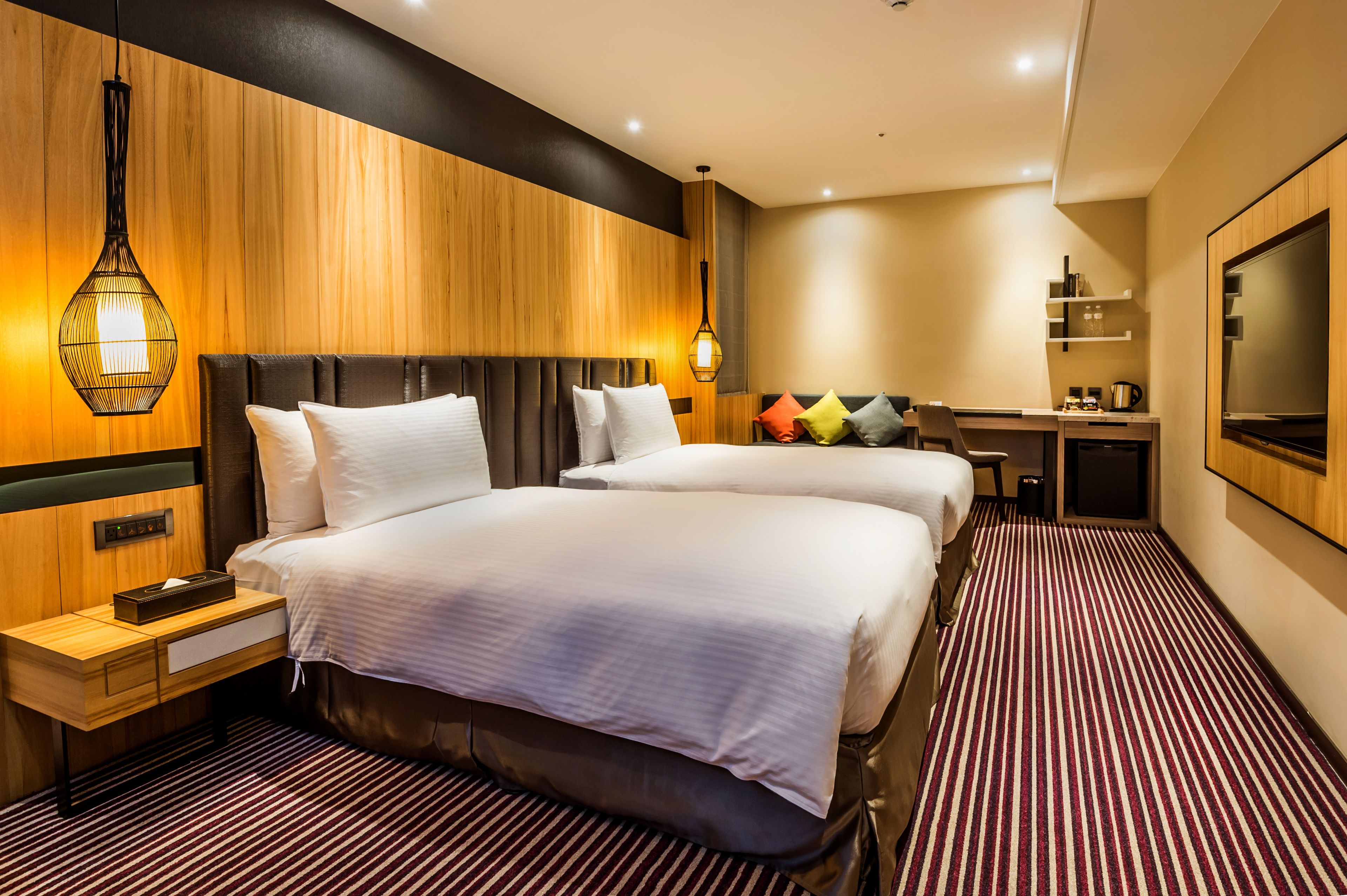 A hotel room with two beds, a desk, a TV, and a minibar.