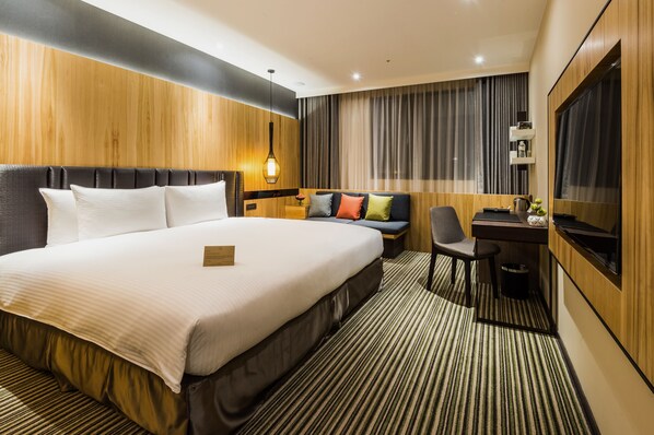 Ein Hotelzimmer mit einem großen Bett, einem Schreibtisch, einem Sessel, einem Fernseher und einer Wand mit Holzverkleidung.