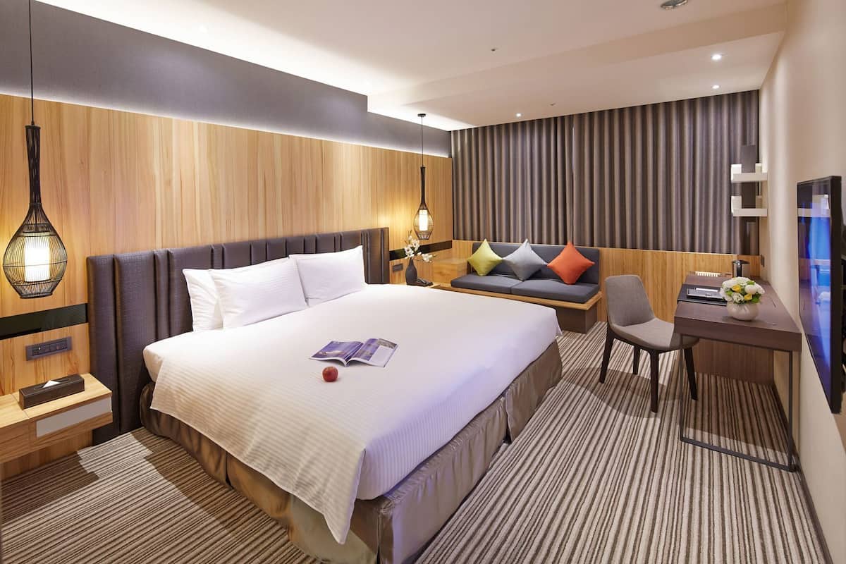 A hotel room with a bed, a desk, a chair, a nightstand, a lamp, and a television.