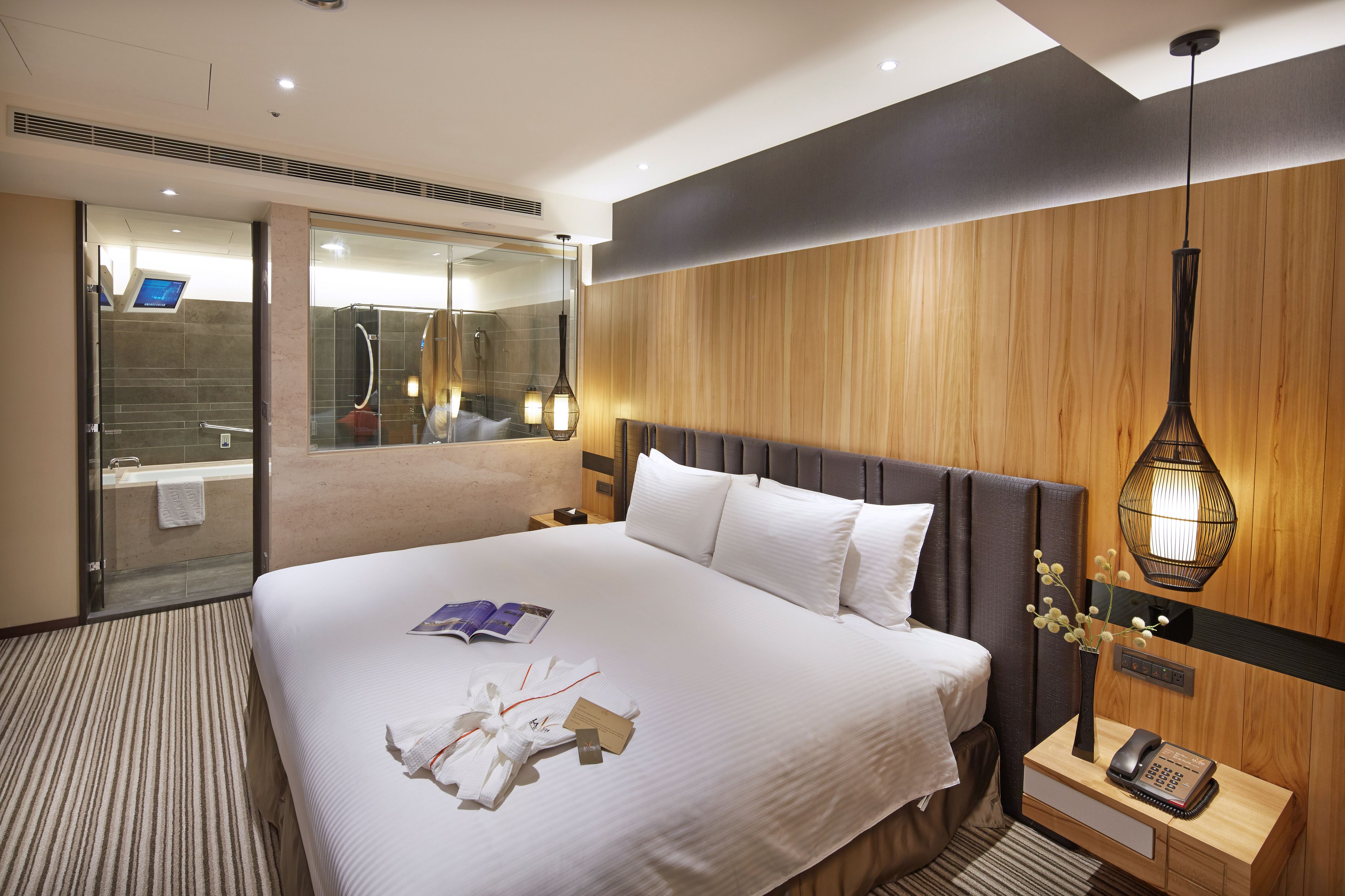 Quarto de hotel com uma cama grande, mesa de cabeceira com telefone, espelho e chuveiro.