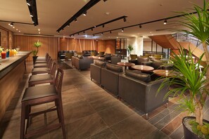 Eine moderne Hotelhalle mit Barbereich, Sitzgelegenheiten und Topfpflanzen.
