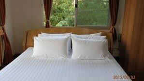 Una cama bien tendida con sábanas y almohadas blancas, un cabecero de madera y una ventana con cortinas.