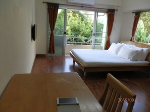 A hotel room with a bed, a table, and a view of greenery through the window.