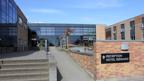 A reception area with a sign for the hotel indgang, a brick wall, and a modern building with glass windows in the background.