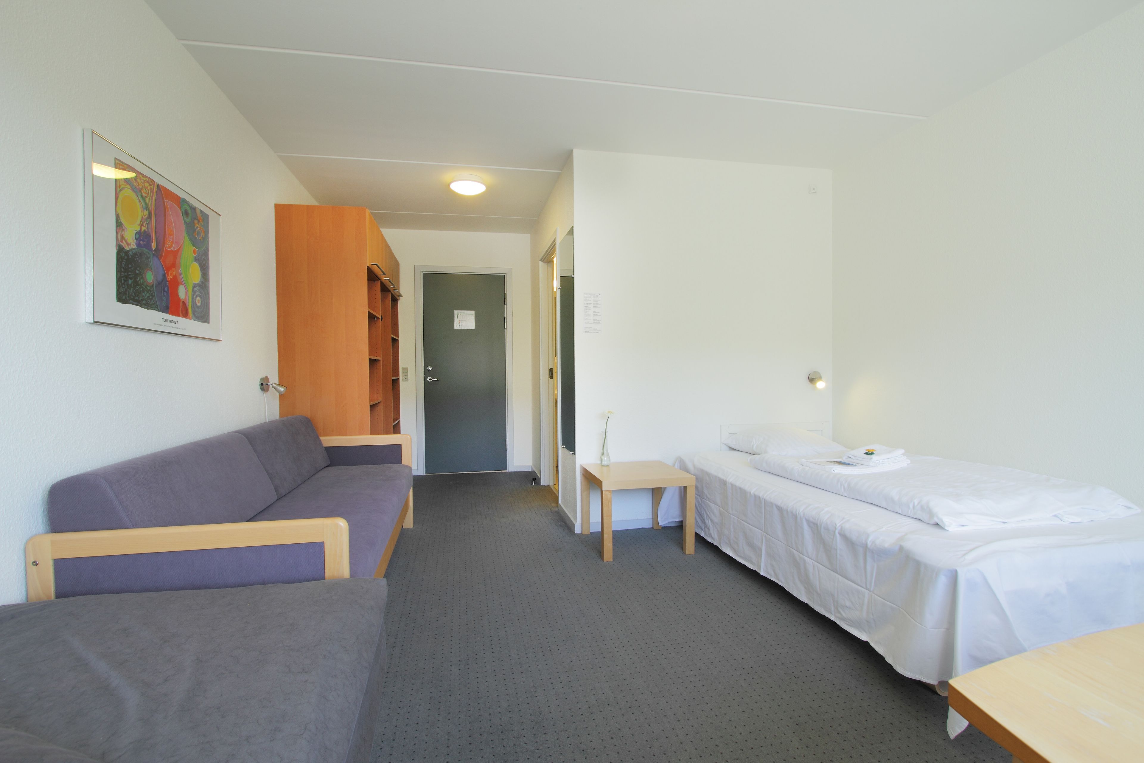 A hotel room with a bed, a small table, a sofa, and a painting on the wall.