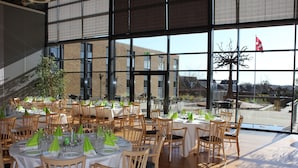 A spacious dining area with round tables set for a meal, large windows offering a view of the outside, and a flag visible through the windows.