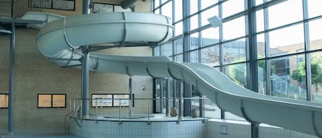 Una piscina interior con dos toboganes y vistas al exterior a través de amplios ventanales.