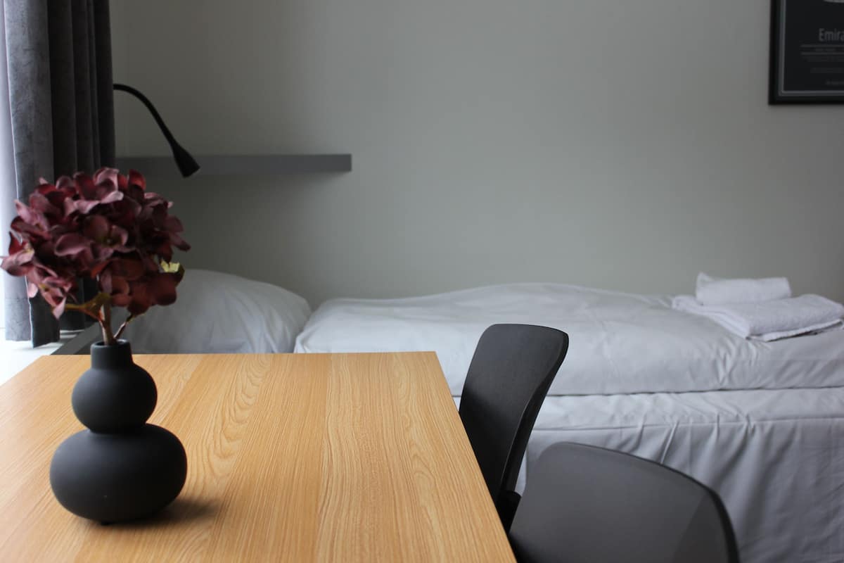 Una habitación de hotel con una mesa de madera, una silla negra, una cama con ropa de cama blanca y un cuadro en la pared.