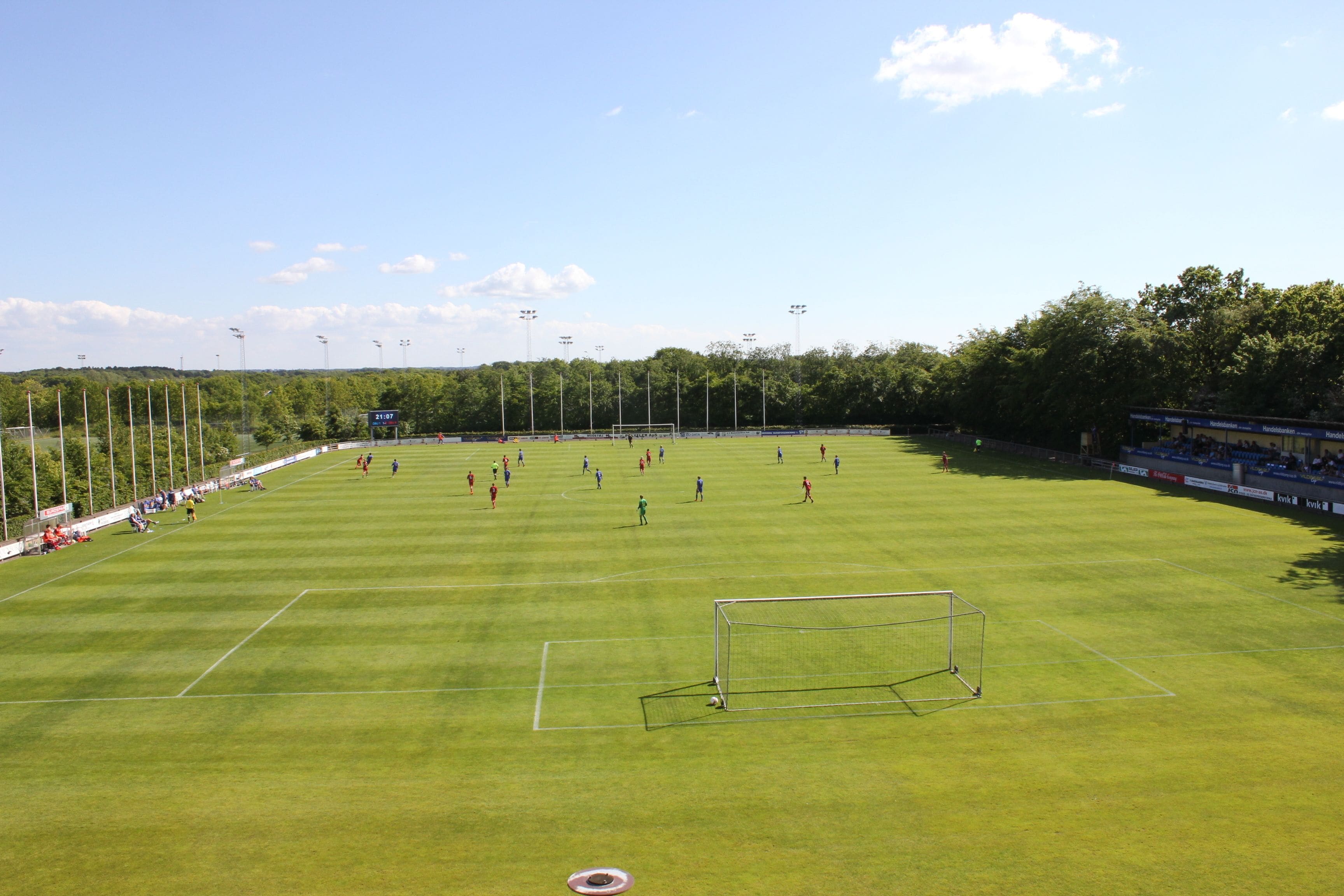 A large, open field with a goalpost, surrounded by trees and a clear sky.