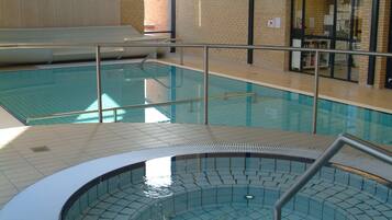 Una piscina interior con bañera de hidromasaje, suelo de baldosas y un reloj en la pared.