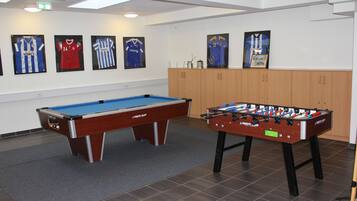 A pool table and a foosball table in a room with framed sports jerseys on the wall.