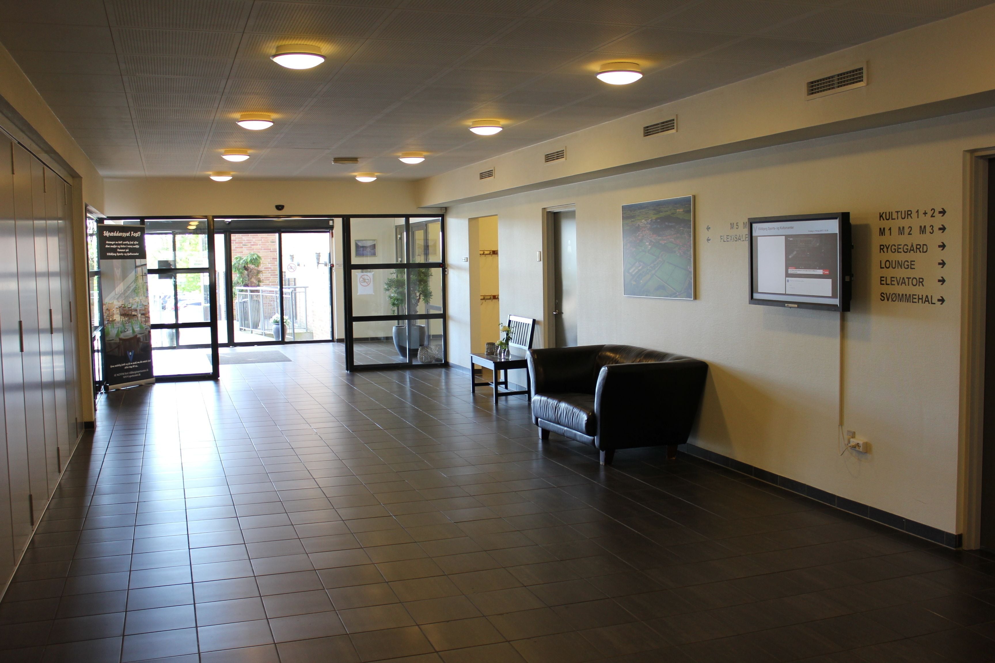 A spacious hallway with a leather sofa, a coffee table, and directional signs on the walls.