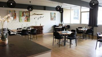 Un comedor moderno con varias mesas y sillas, una pared de ladrillo con obras de arte y ventanas amplias con cortinas.