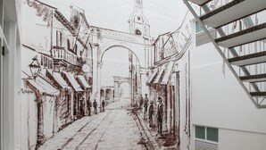 Un pasillo con un mural de una escena callejera, una escalera y plantas en macetas.