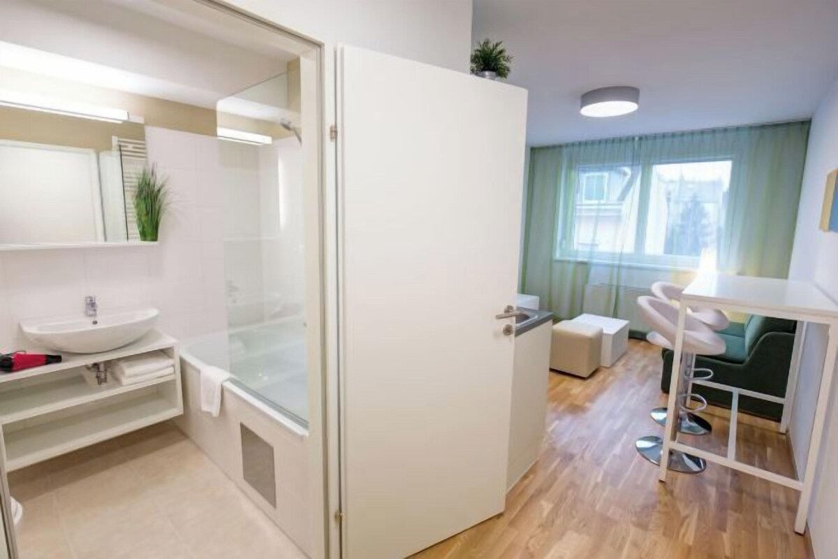 A modern bathroom with a glass shower enclosure, a white sink, and a small stool.