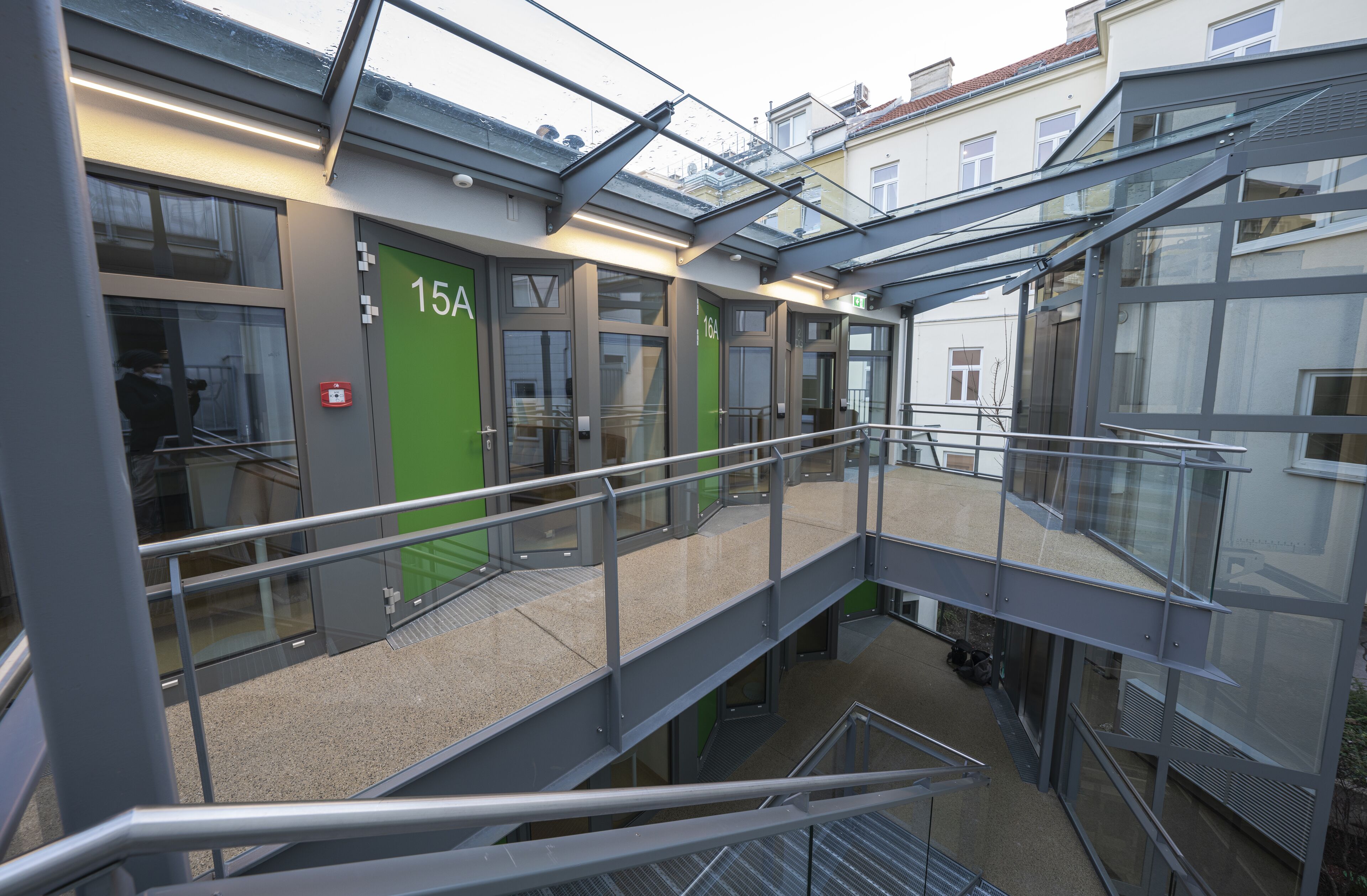 A modern building with multiple floors, glass railings, and numbered doors.