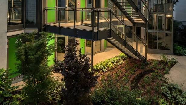 Un edificio moderno con una scalinata in vetro che collega diversi piani, immerso nel verde.