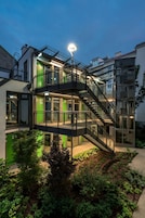 Een modern gebouw met een glazen wenteltrap die verschillende verdiepingen met elkaar verbindt, omringd door groen.