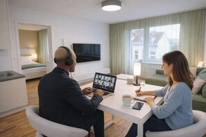 Una habitación de hotel moderna con un escritorio, una computadora portátil, un televisor y una zona de estar confortable.
