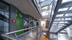 Una scala interna con ringhiere in metallo e un soffitto in vetro che conduce a un corridoio con una porta verde con la scritta '10A'.