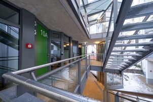 An indoor staircase with metal railings and a glass ceiling, leading to a corridor with a green door labeled "10A".