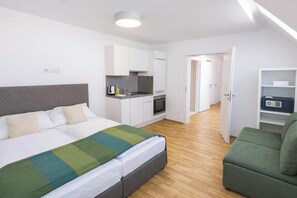 Ein modernes Hotelzimmer mit Bett, Küchenzeile und einem grünen Sessel.