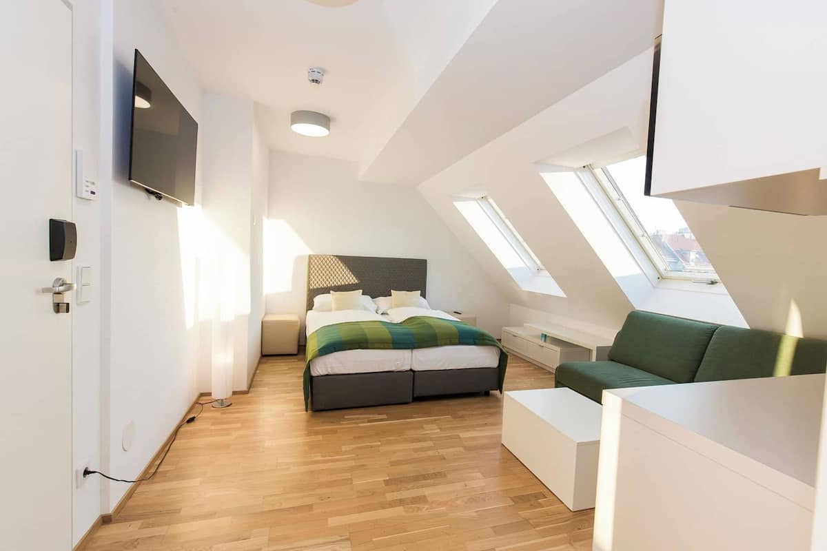 A modern, well-lit room with a bed, a green sofa, and a white desk.