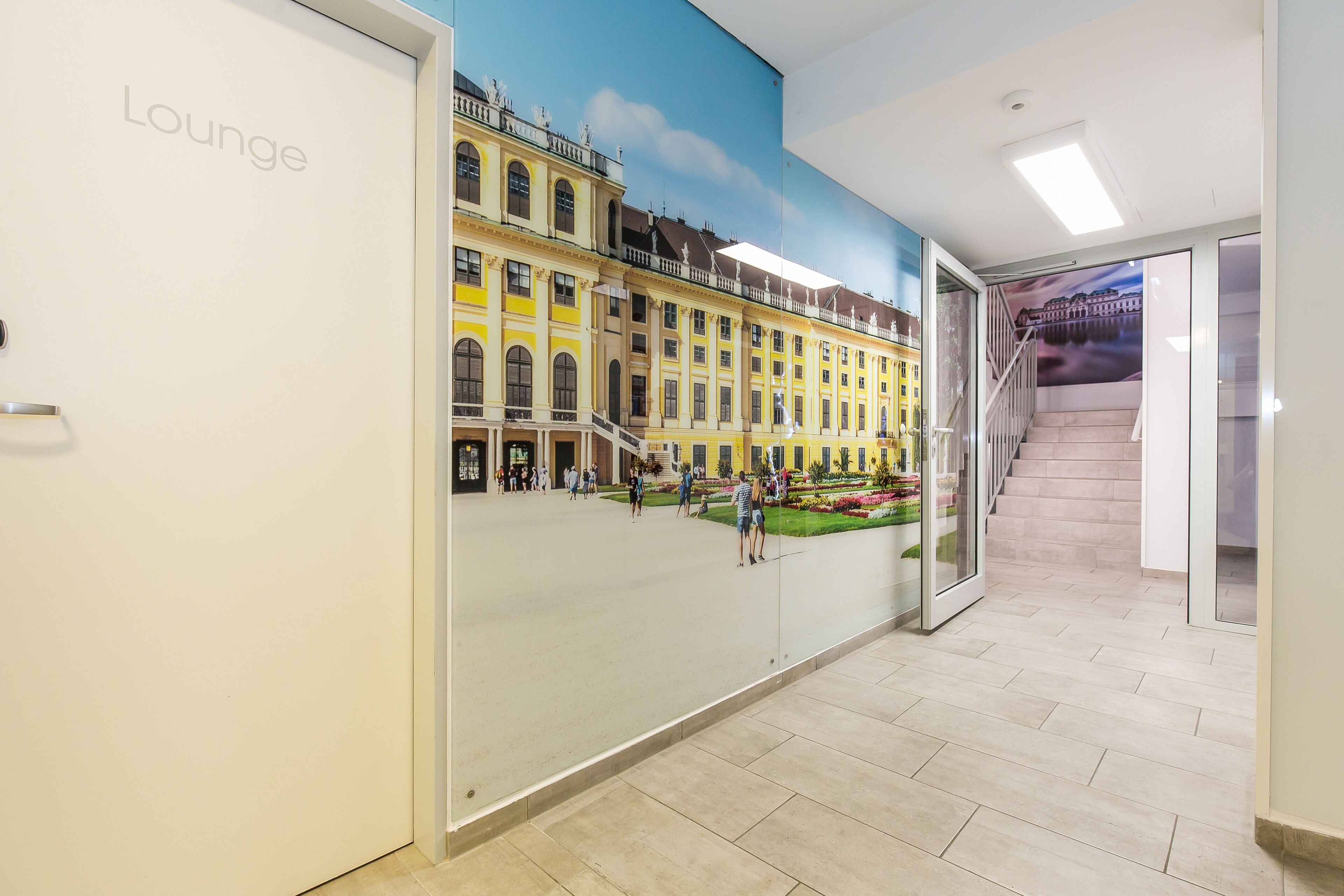 A lounge area with a mural of a historic building, a staircase, and a tiled floor.