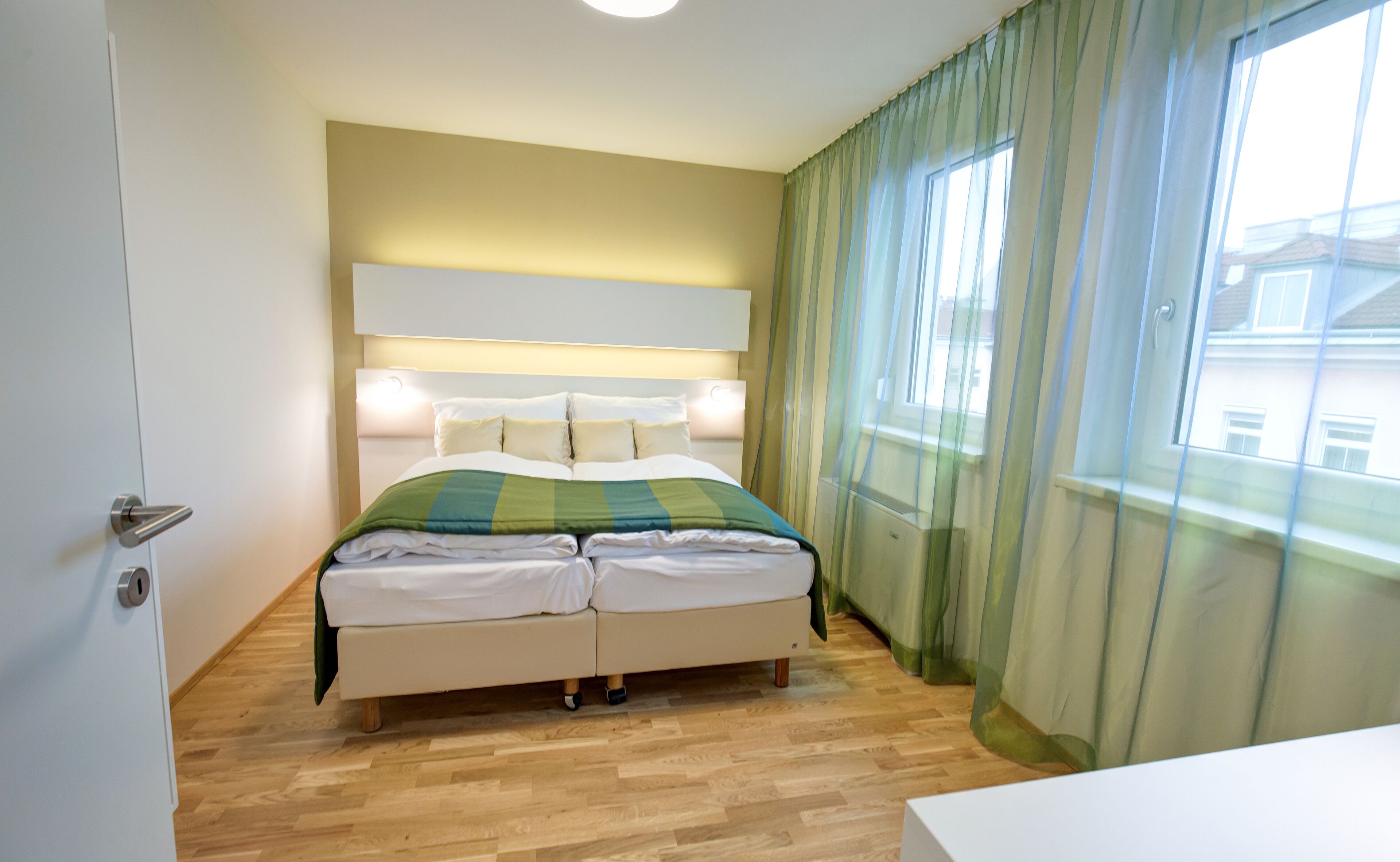 Een slaapkamer met een bed, een hoofdbord, een raam met gordijnen en een houten vloer.