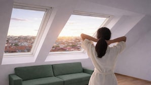 Una stanza con un divano verde, due lucernari e vista sulla città.
