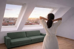Una stanza con un divano verde, due lucernari e vista sulla città.