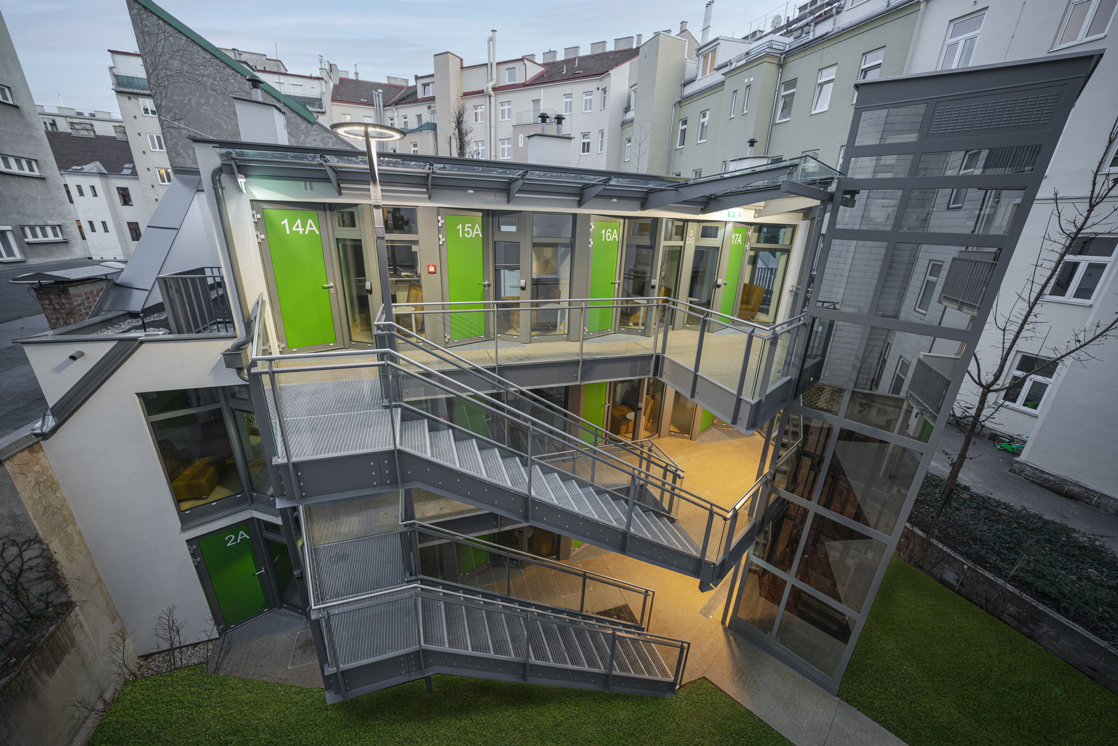 A multi-level building with glass railings and green doors, featuring a staircase and multiple entry points.