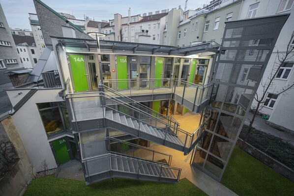 A multi-level building with glass railings and green doors, featuring a staircase and multiple entry points.