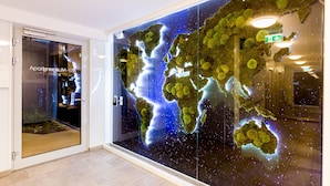 Interno moderno di un hotel con un'ampia mappa del mondo dipinta, un ingresso con porta in vetro e un ascensore ben visibile.