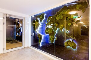 Een modern hotelinterieur met een grote wereldkaart op de muur, een glazen deur en een zichtbare lift.