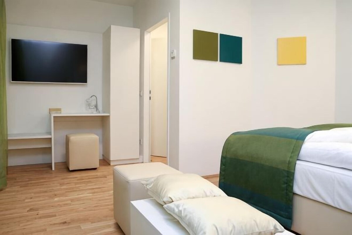 A bedroom with a bed, a desk, a chair, and a television.
