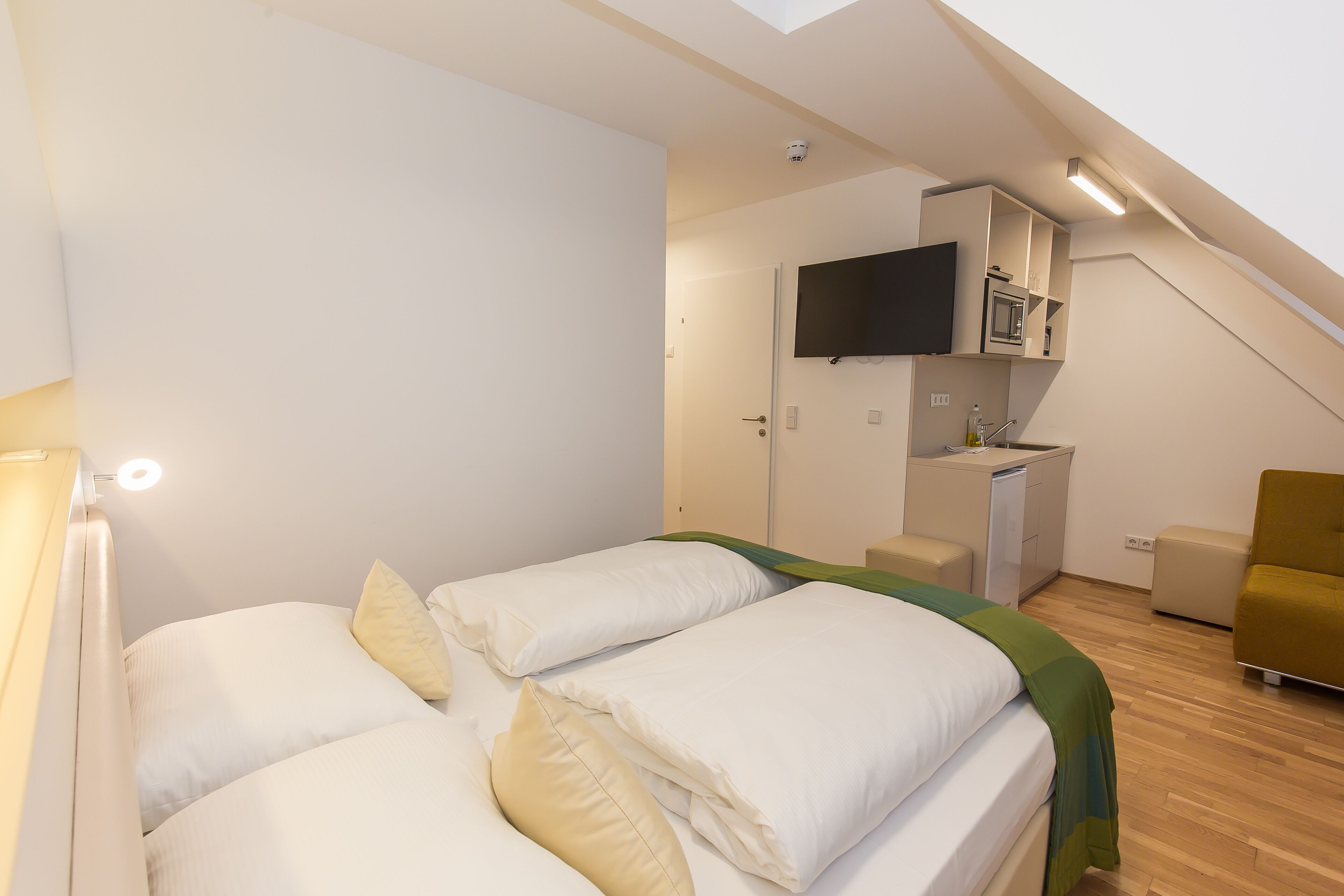 Une chambre avec deux lits, une télévision, un coin cuisine et une chaise.