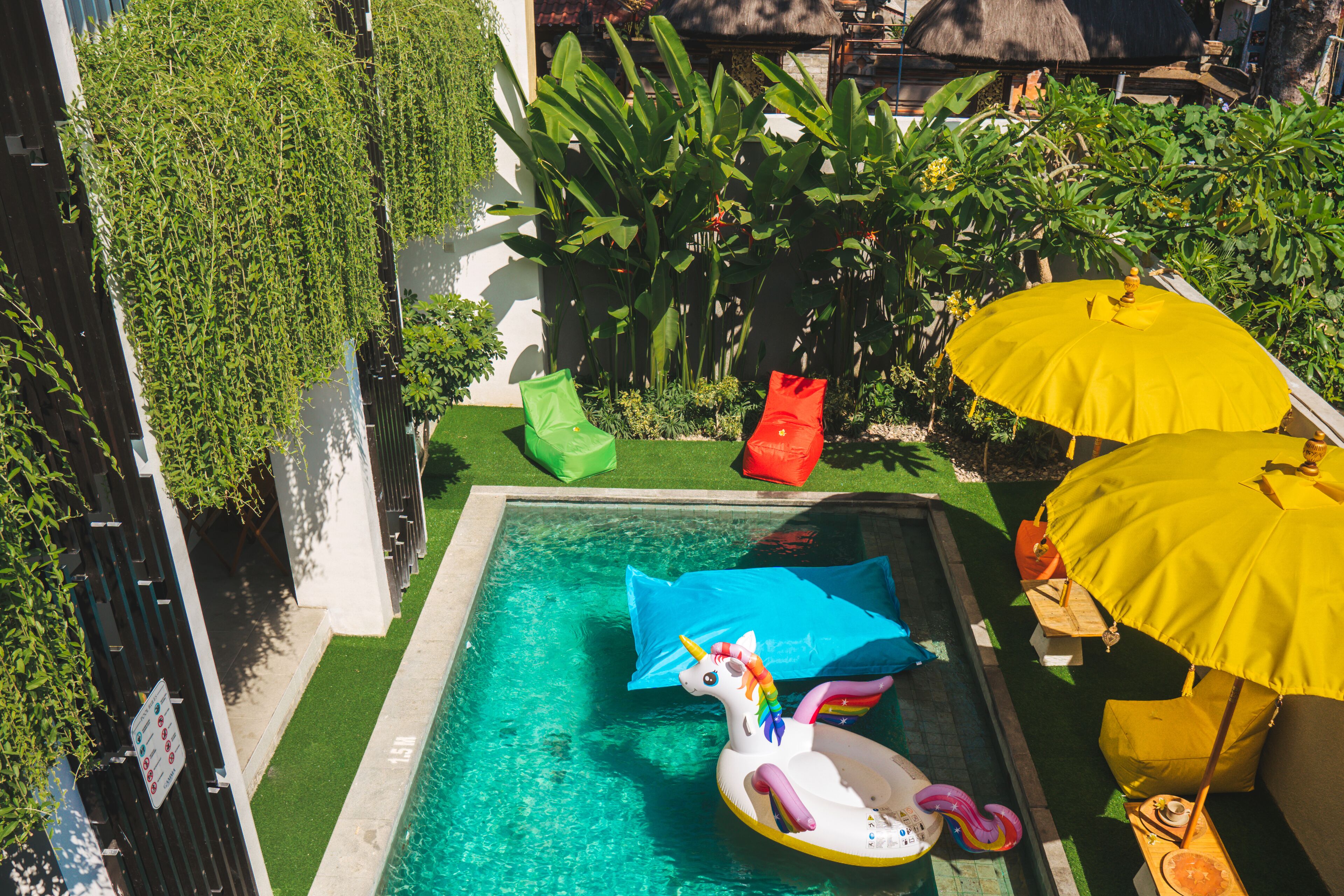 A swimming pool with a unicorn float, surrounded by greenery and yellow umbrellas.